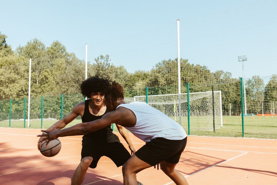 Two young men playing basketball on an outdoor court on a sunny day.