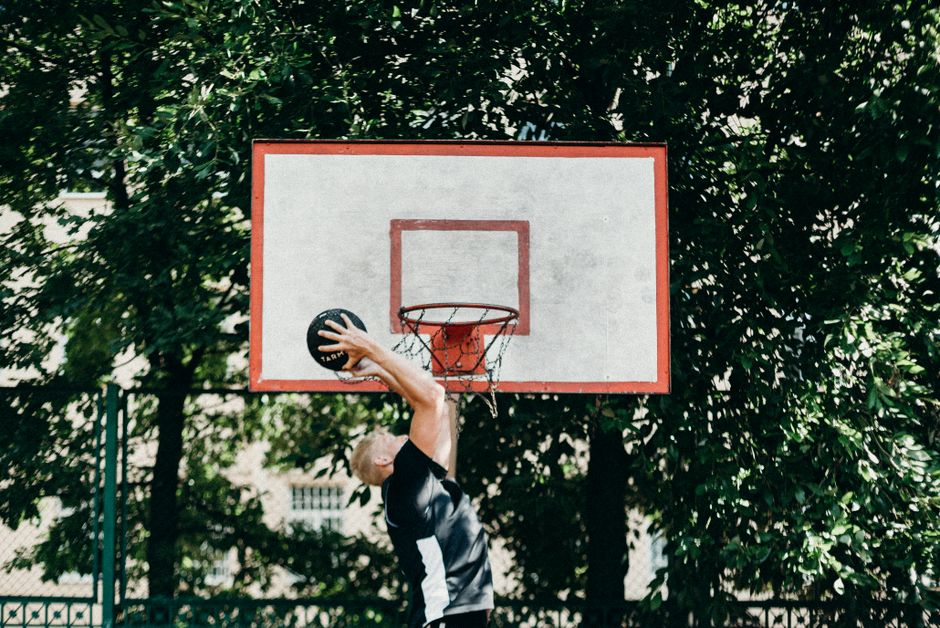 A man performing a slam dunk on an outdoor basketball court amidst lush greenery.