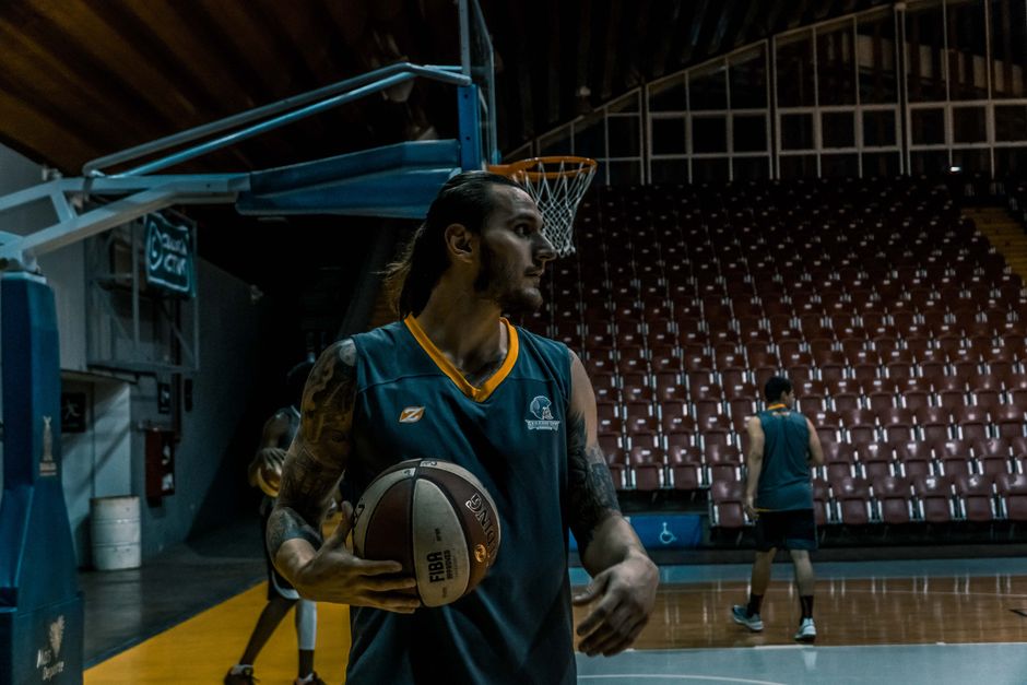 Male basketball players training and practicing in an indoor gym with basketballs and hoops.
