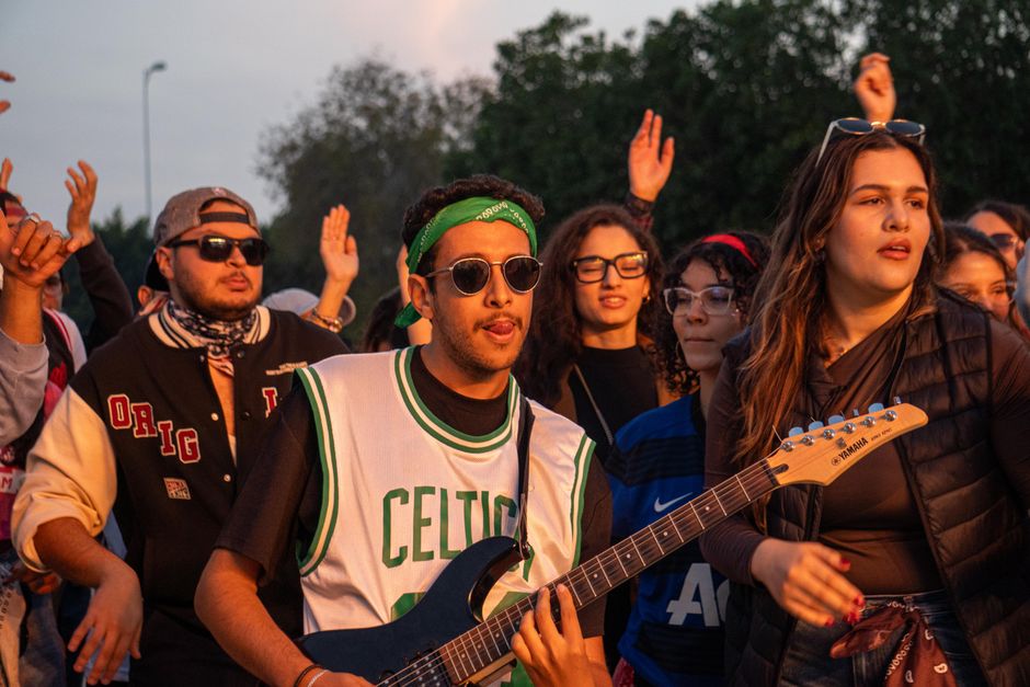 Energetic outdoor music event featuring young adults enjoying a live performance with guitars.