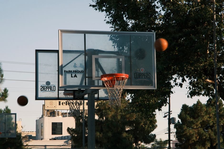 A basketball hoop on an outdoor court in Los Angeles, with trees and buildings in the background.