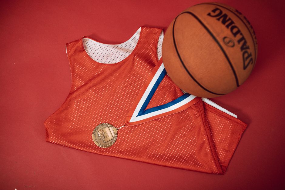 A red basketball jersey paired with a medal and Spalding basketball on a red backdrop.