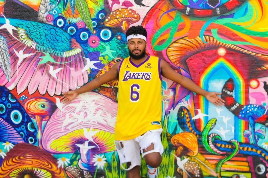 Man in Lakers jersey posing against a colorful mural wall, showcasing vibrant art and style.