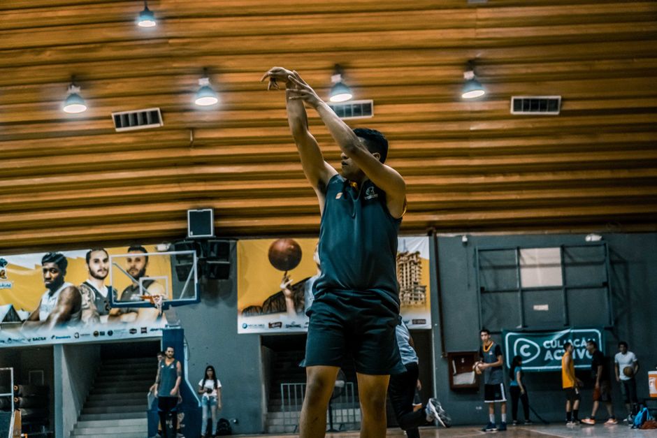 A basketball player takes a shot during practice in an indoor gymnasium setting.
