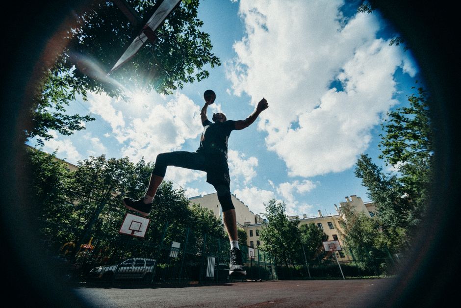 Silhouette of a basketball player making a dramatic jump shot under a clear sky.