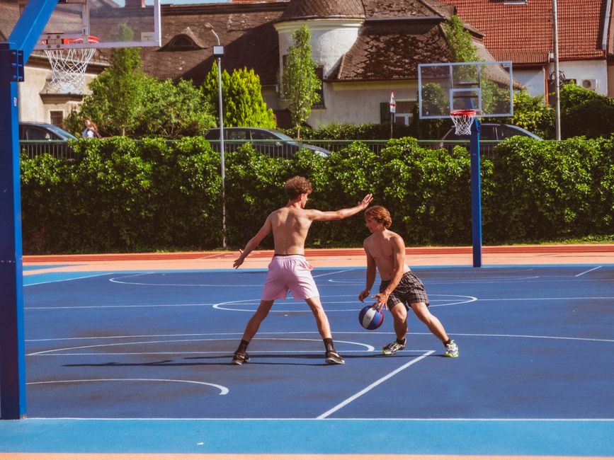 Two young men playing basketball on an outdoor court on a sunny day.