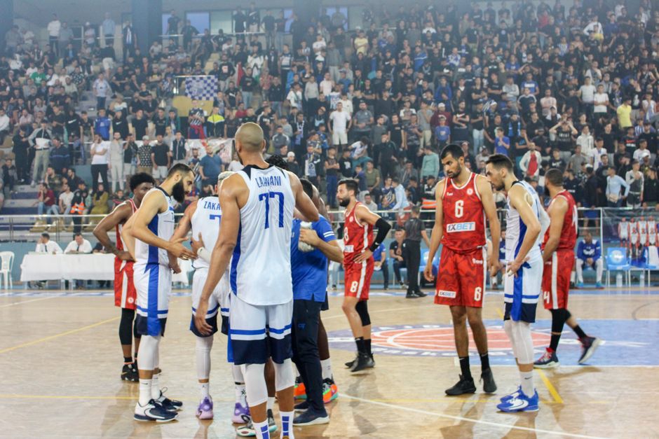Basketball players in action during a competitive match with a full stadium crowd.