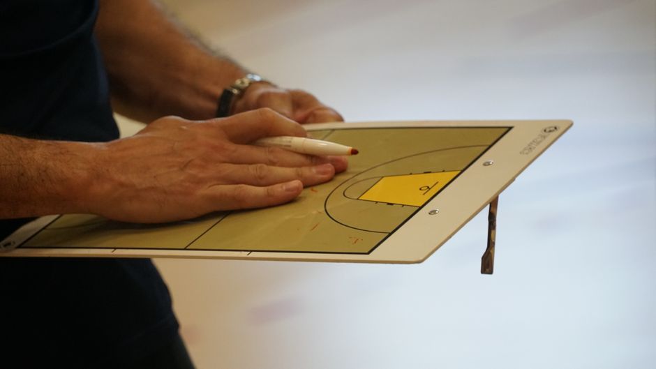 Close-up of a coach using a basketball tactics board to plan game strategy indoors.