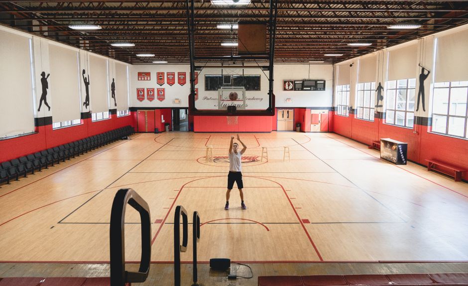 Athlete practicing basketball shots in a spacious indoor gym with wooden flooring.