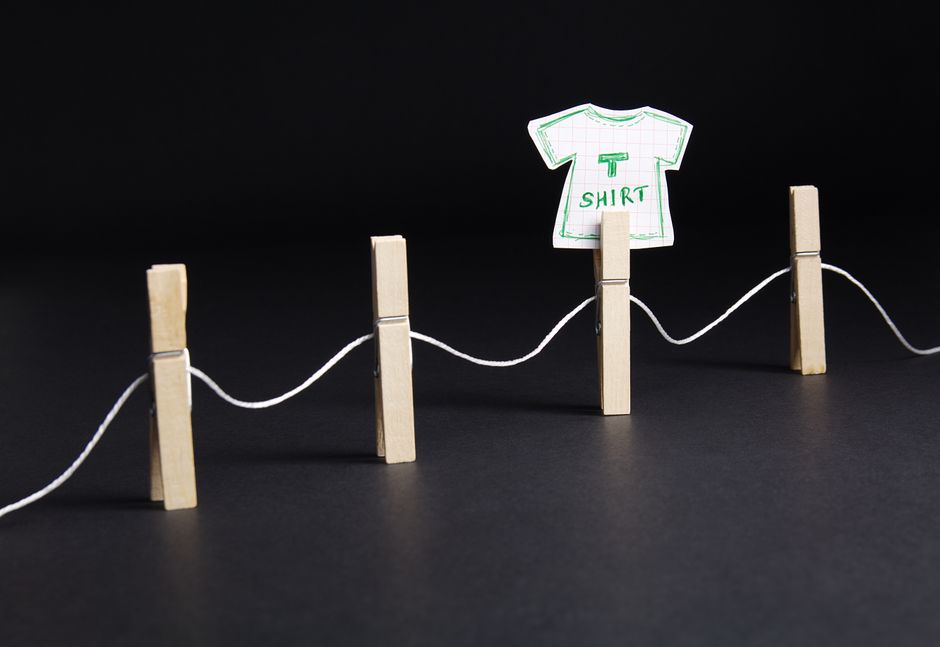 Artistic depiction of a paper t-shirt hung on a clothesline with wooden pins against a dark background.