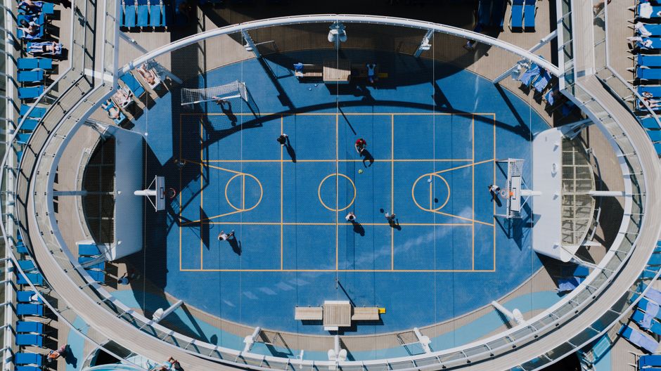 Aerial view of a basketball game on a cruise ship with players, hoops, and spectators.